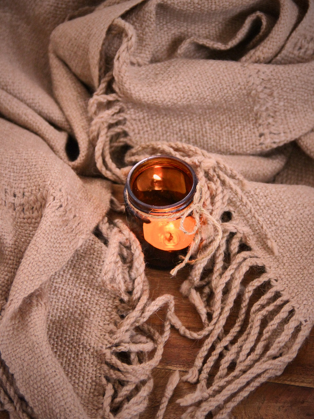 Brauner Schal mit einer Kerze in einem Glasgefäß auf einer Holzfläche 