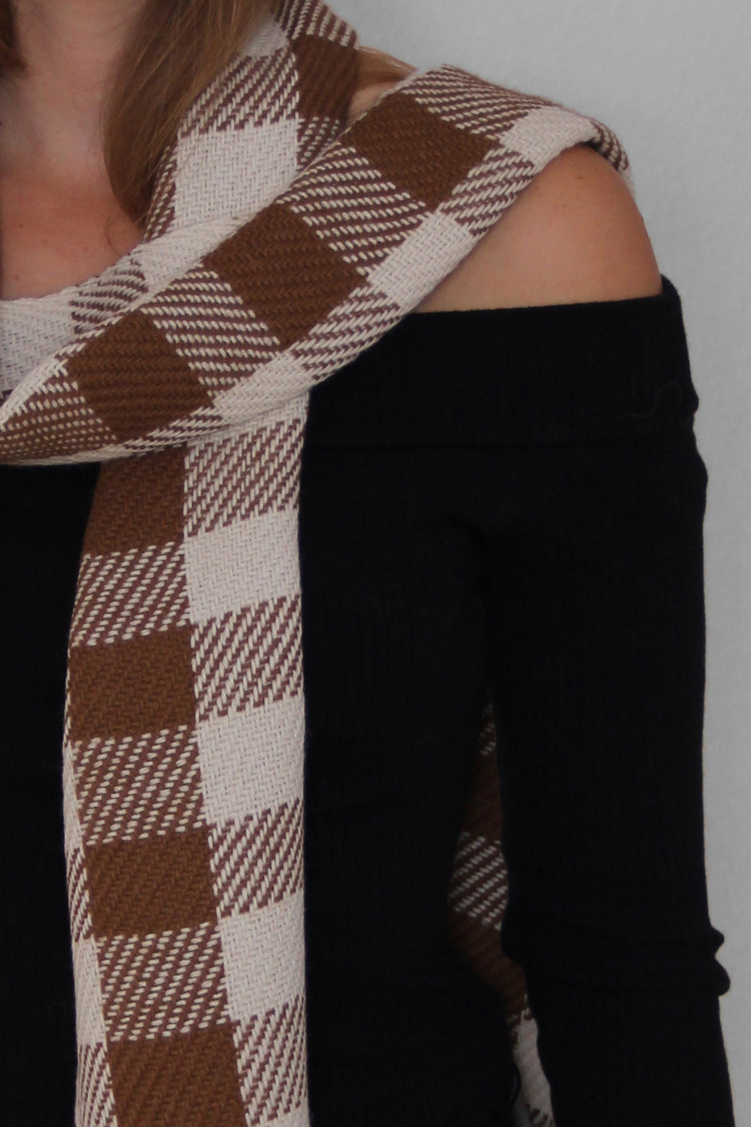 Blondes Model trägt einen karierten Schal aus Alpakawolle in braunen und weißen Farben. Nahaufnahme