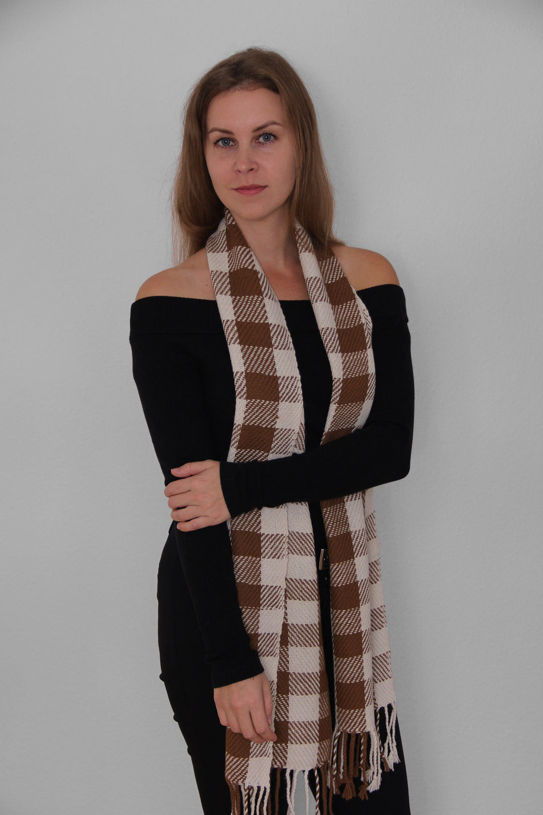 Blondes Model trägt einen karierten Schal aus Alpakawolle in braunen und weißen Farben.